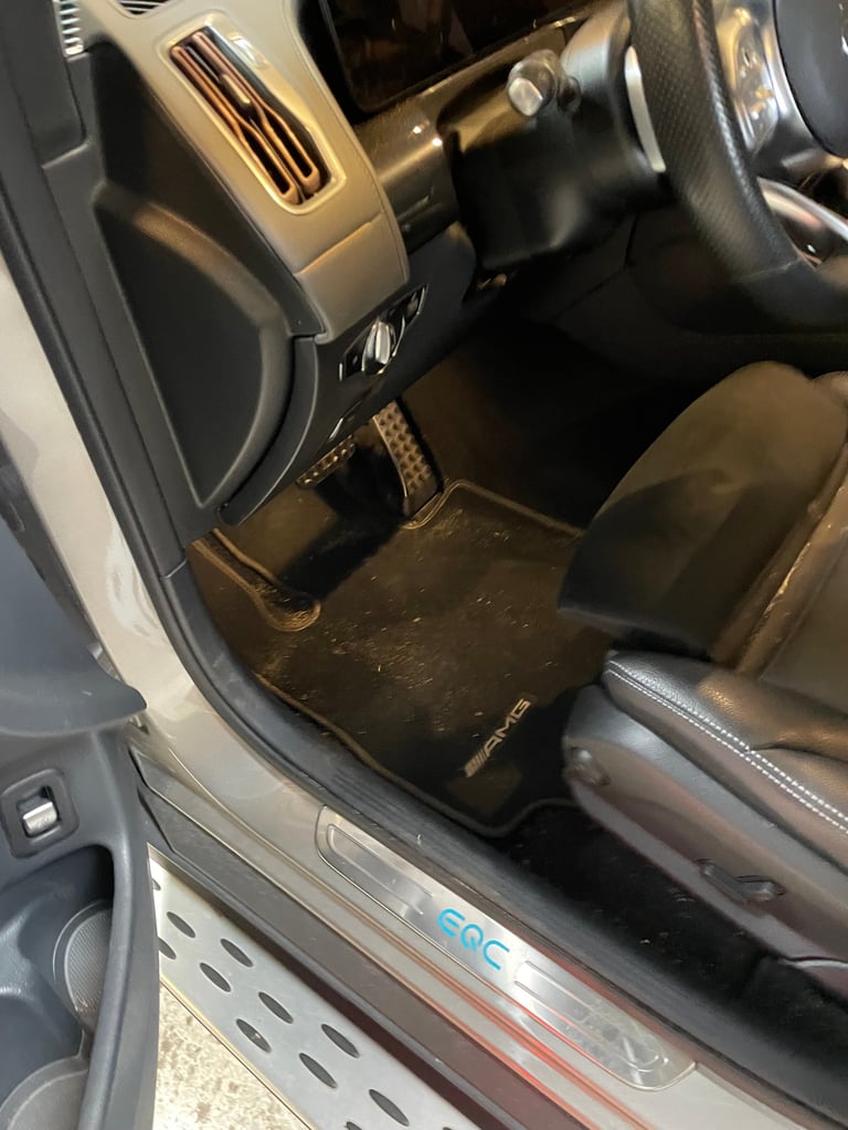 Car interior showing drivers seat, steering wheel, dashboard and black floor mats
