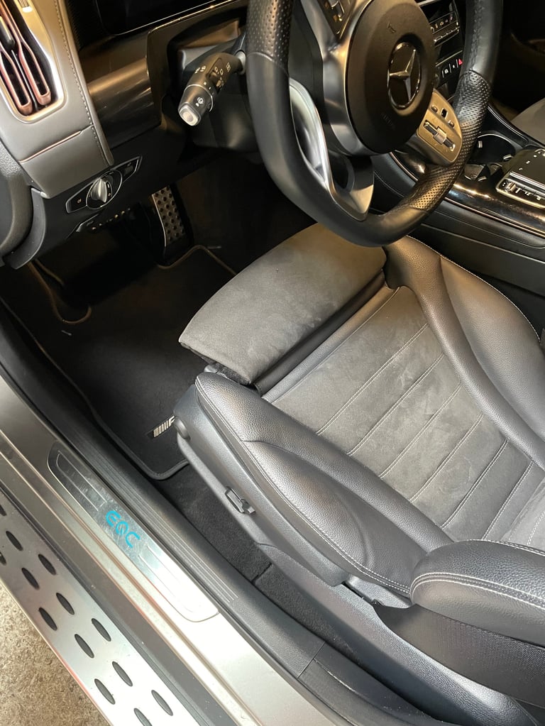 Car interior showing black leather steering wheel, gray upholstered drivers seat and dashboard from above