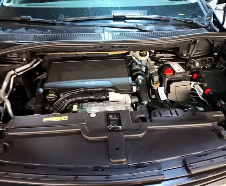 Open car engine bay showing motor, battery, hoses, and mechanical components