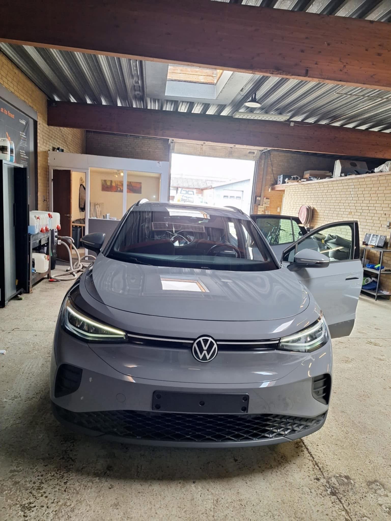 Gray Volkswagen electric vehicle parked in an automotive service garage with open door and corrugated metal roof