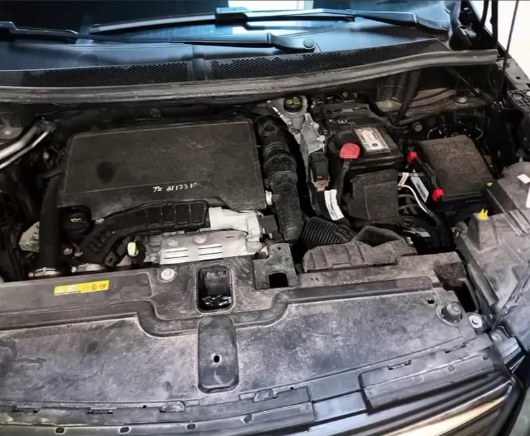 Open car engine compartment showing motor components, battery, and wiring harness