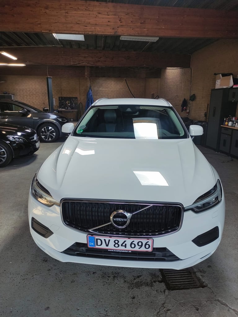 White Volvo sedan with black grille parked in garage with license plate DV 84696