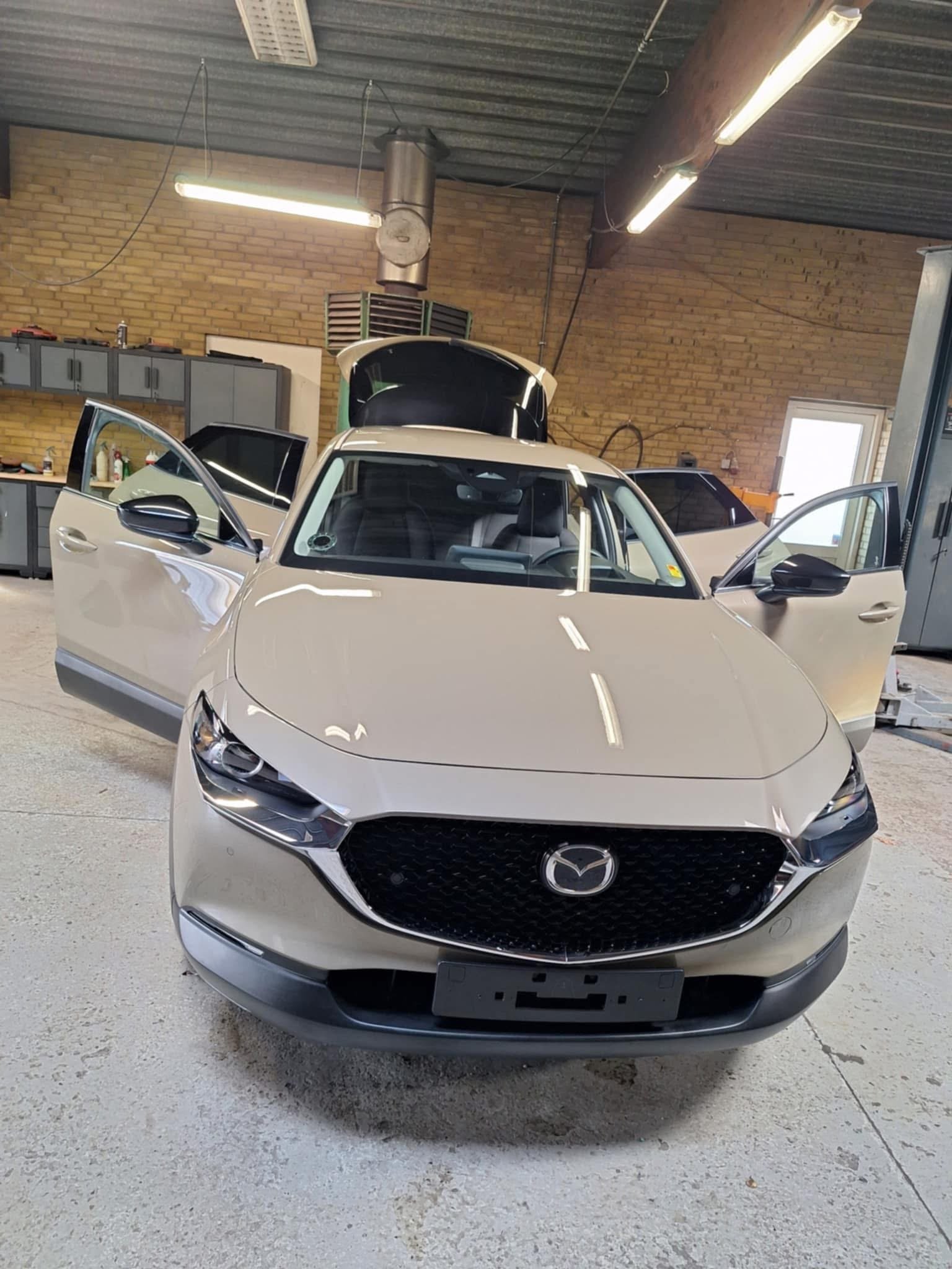 White Mazda sedan on display in a brick garage with open doors, showing front view with LED ceiling lights